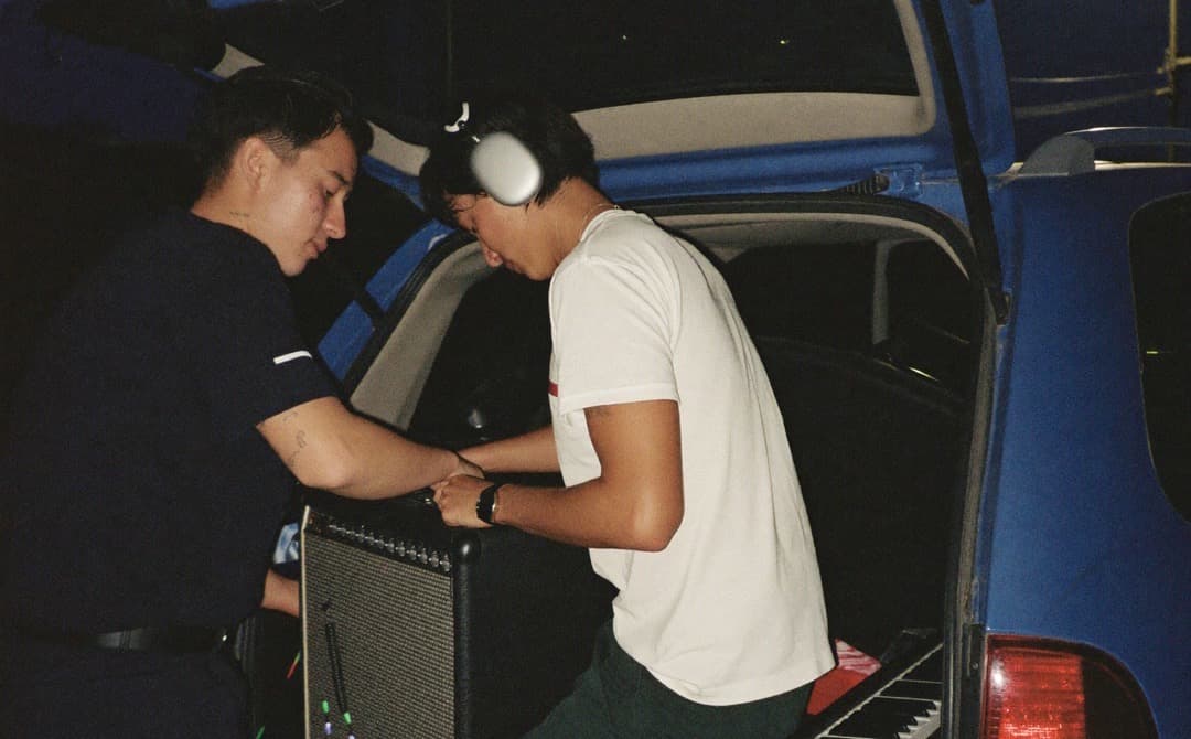 Two musicians loading gear into a hatchback at night