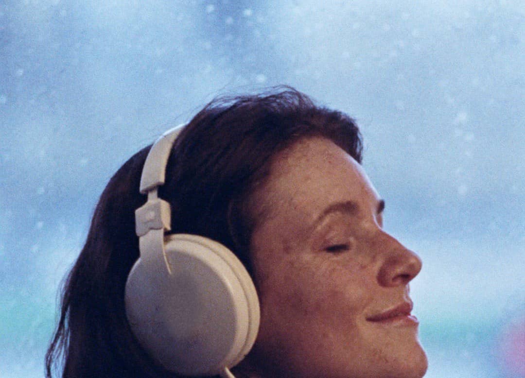 A listener in headphones, eyes closed, by a rainy window